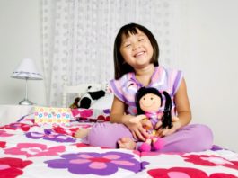 Girl sitting on bed with doll.