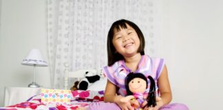 Girl sitting on bed with doll.