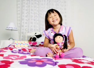 Girl sitting on bed with doll.
