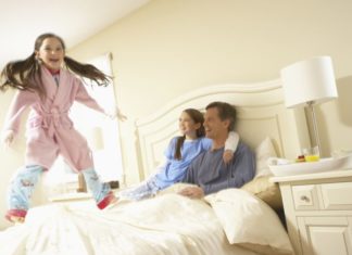 A girl jumps on the bed as her parents look on smiling.