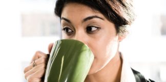 Woman drinking coffee from a green mug.