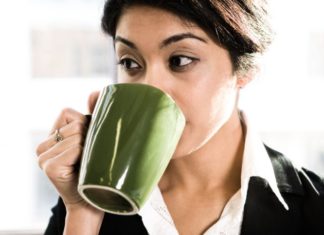 Woman drinking coffee from a green mug.