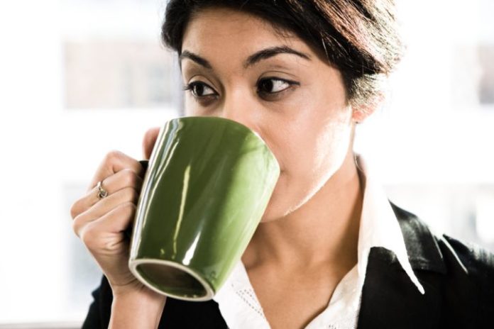 Woman drinking coffee from a green mug.