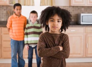 Angry girl in kitchen with two boys in background.