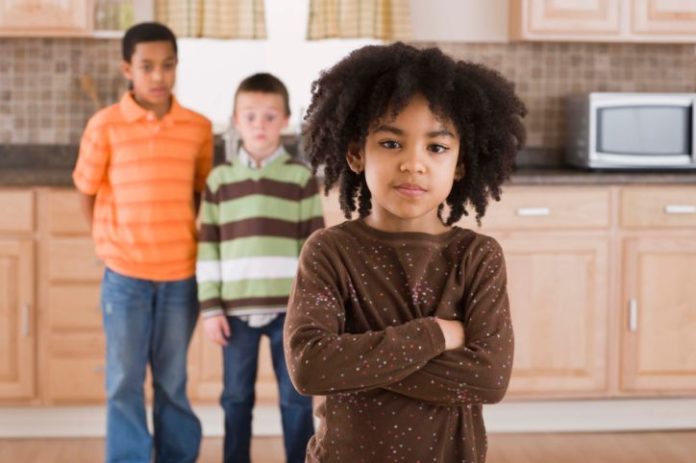 Angry girl in kitchen with two boys in background.