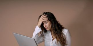 Woman sits with laptop on knees. She is distressed.