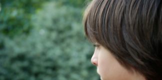 Side view of a boy looking out toward greenery.