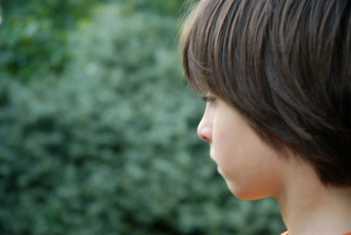 Side view of a boy looking out toward greenery.