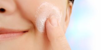 A close shot of a woman applying lotion to her cheek.