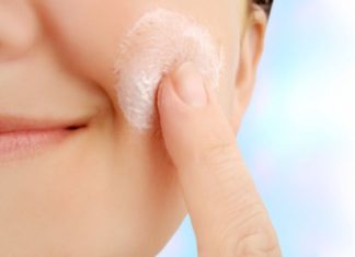 A close shot of a woman applying lotion to her cheek.