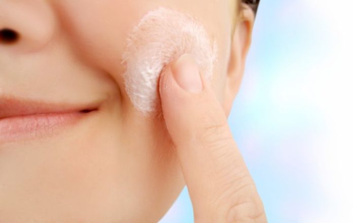 A close shot of a woman applying lotion to her cheek.