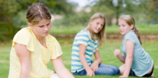 Two young girls bullying other young girl outdoors