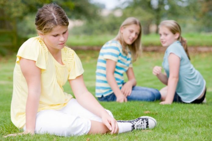 Two young girls bullying other young girl outdoors