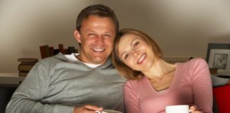 Couple with coffee mugs sitting on a couch.