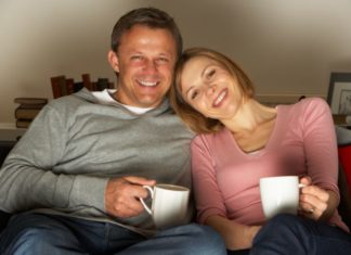 Couple with coffee mugs sitting on a couch.