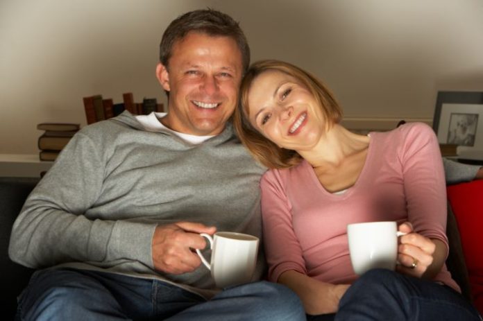 Couple with coffee mugs sitting on a couch.