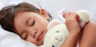 Sleeping little girl holding white teddy.