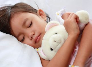 Sleeping little girl holding white teddy.