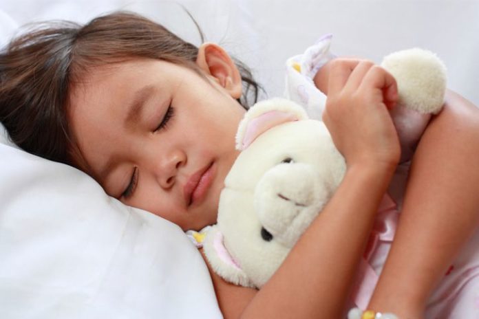 Sleeping little girl holding white teddy.