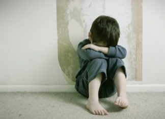 Sad boy, curled up on floor in front of wall.