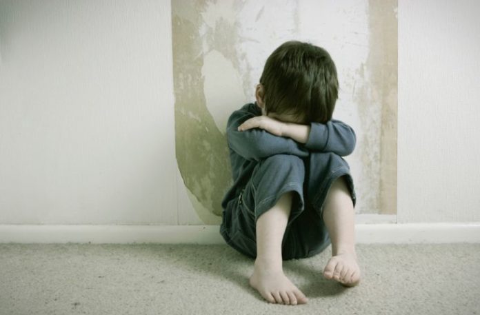 Sad boy, curled up on floor in front of wall.