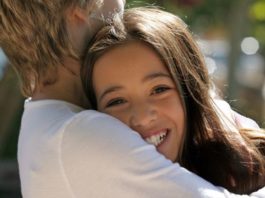 A teenage couple hug. The girl's face is to camera.