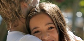 A teenage couple hug. The girl's face is to camera.