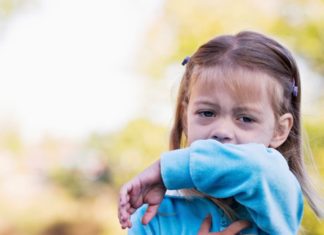 A little girl coughs into her sleeve.