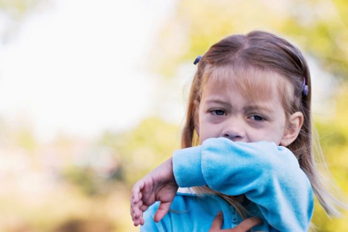 A little girl coughs into her sleeve.