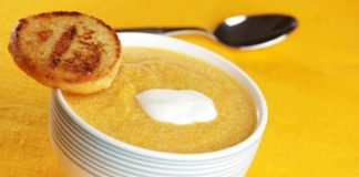 A small bowl of pumpkin soup with a dash of yogurt on top and a small piece of toast balanced precariously in the edge of the bowl.