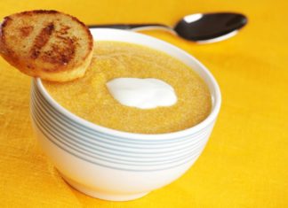 A small bowl of pumpkin soup with a dash of yogurt on top and a small piece of toast balanced precariously in the edge of the bowl.