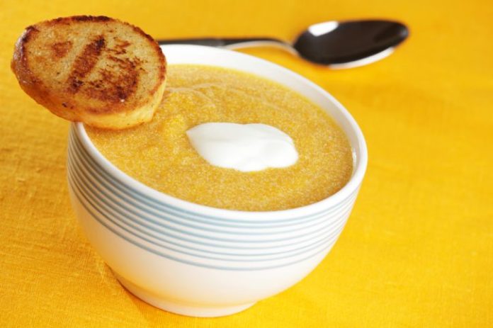 A small bowl of pumpkin soup with a dash of yogurt on top and a small piece of toast balanced precariously in the edge of the bowl.