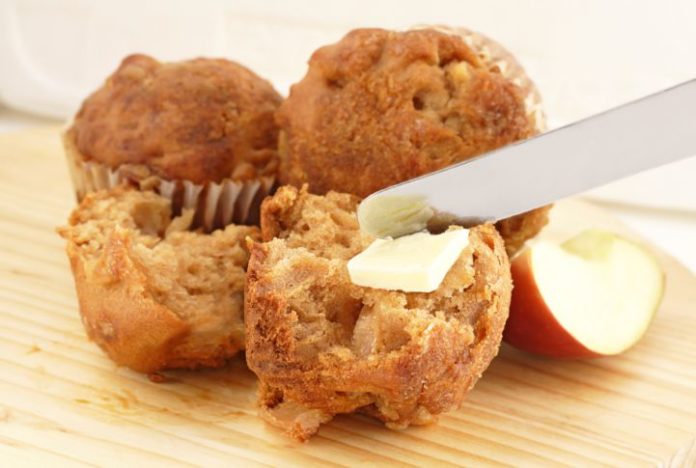 Tasty looking apple bran muffins being spread with butter.