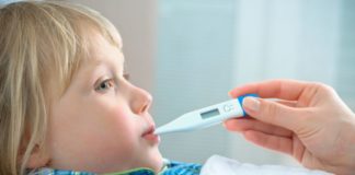 A hand holding a thermometer in a boy's mouth. The boy is in bed.