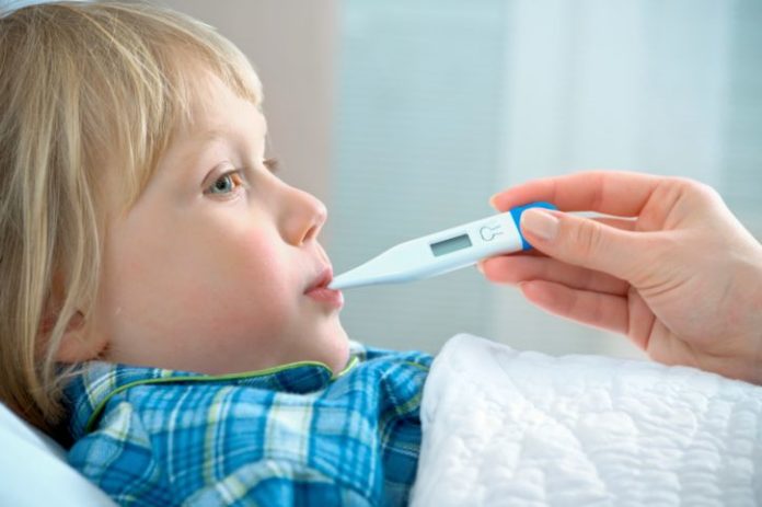 A hand holding a thermometer in a boy's mouth. The boy is in bed.