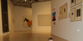 A little girl crawling on the floor of the art gallery, looks up to admire the paintings.