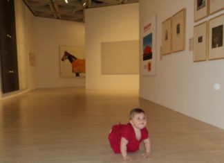 A little girl crawling on the floor of the art gallery, looks up to admire the paintings.