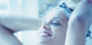 A woman smiles as she lathers her hair with shampoo.