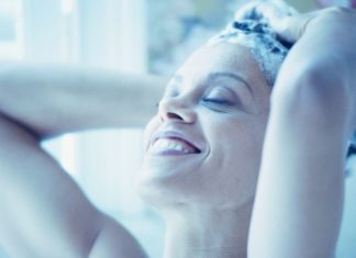 A woman smiles as she lathers her hair with shampoo.