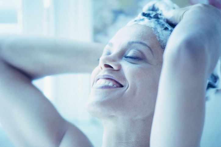 A woman smiles as she lathers her hair with shampoo.