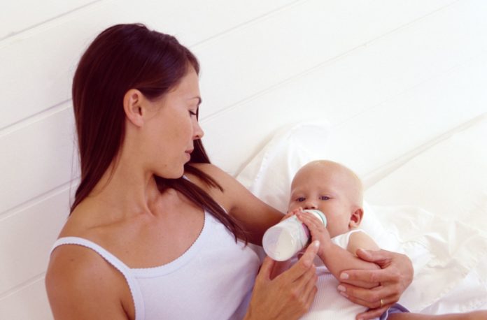 Woman feeding hungry baby with bottle.