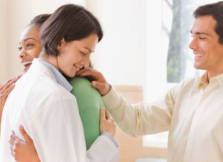 A happy couple hug a female doctor.