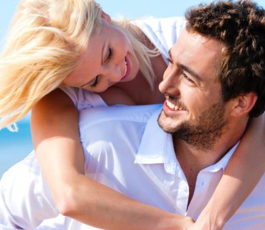 A woman on a man's back with blue skies behind them.