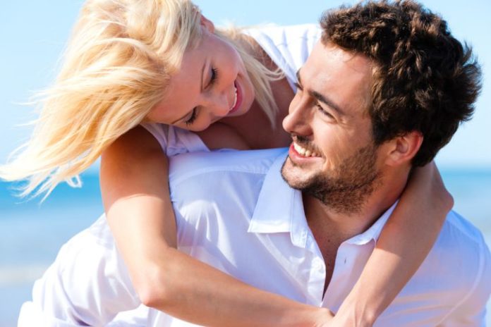 A woman on a man's back with blue skies behind them.