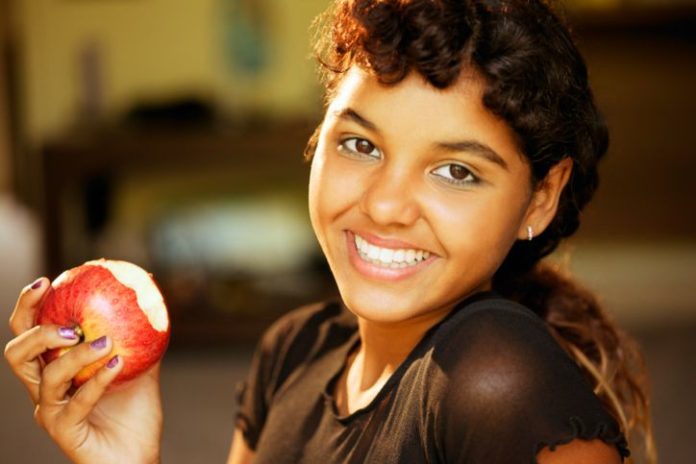 Beautiful smiling girl eating an apple.