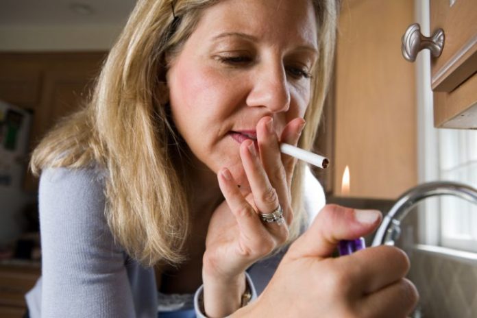 A woman looking a little desperate goes to light a cigarette. She is at home, in the kitchen.